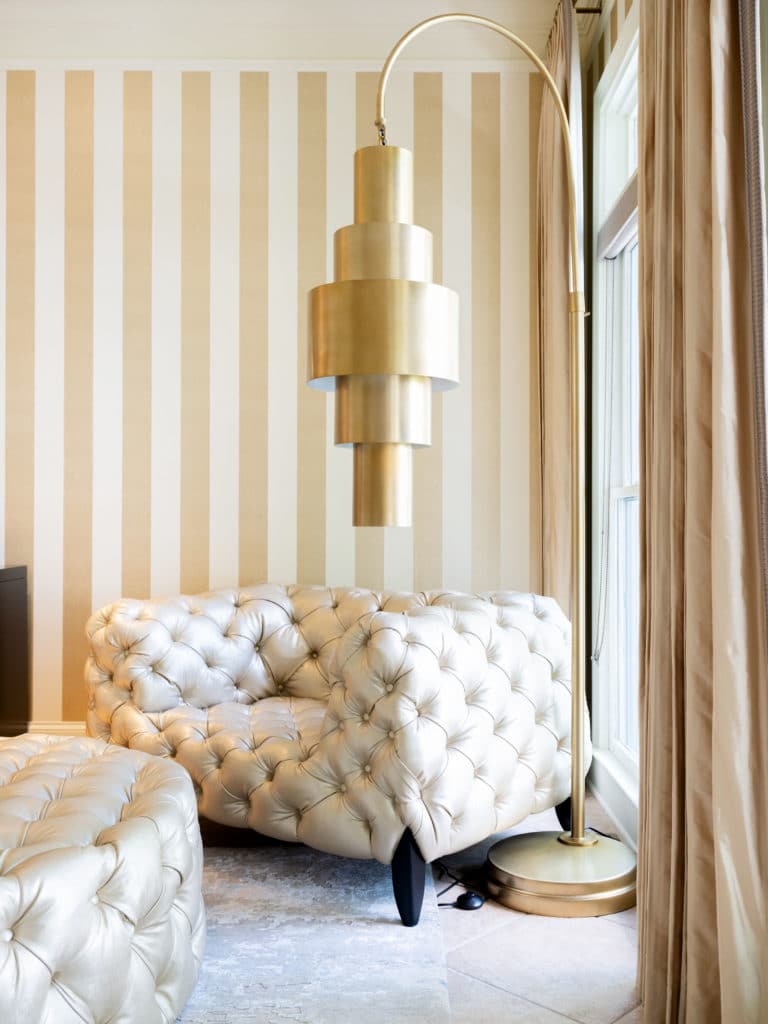 Gold and white striped wall, with oversized gold floor lamp, and tufted chair