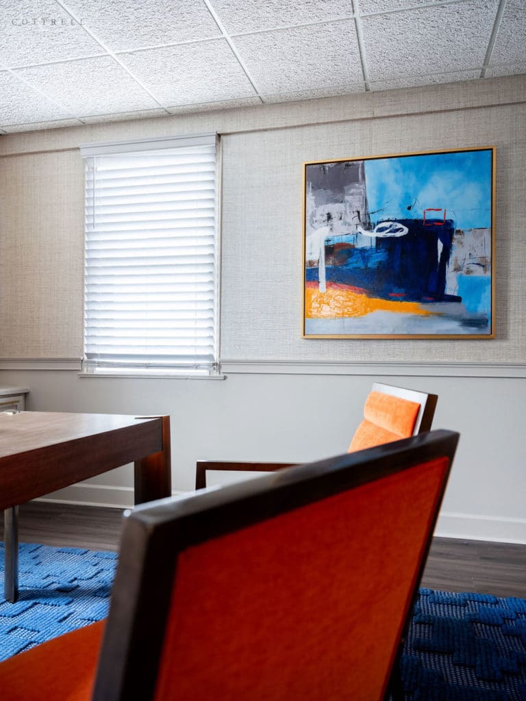 Home office with orange chairs, blue textured rug, and sleek artwork.